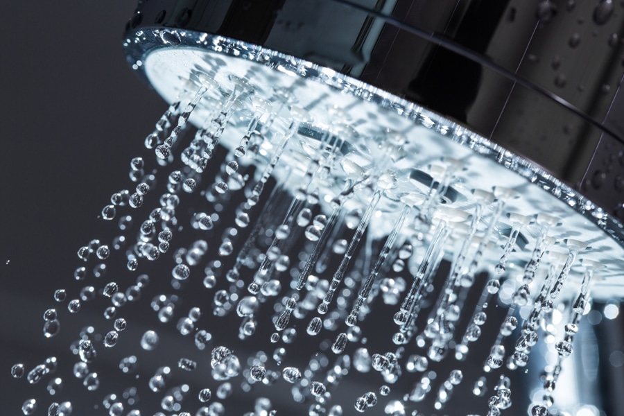Shower Head with Water Stream on Black Background. Should I buy a tankless water heater instead.